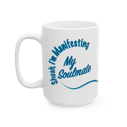 A white ceramic coffee mug with a blue printed graphic that reads 'Shush, I'm Manifesting My Soulmate' in a stylized script font, shown on a plain white background.