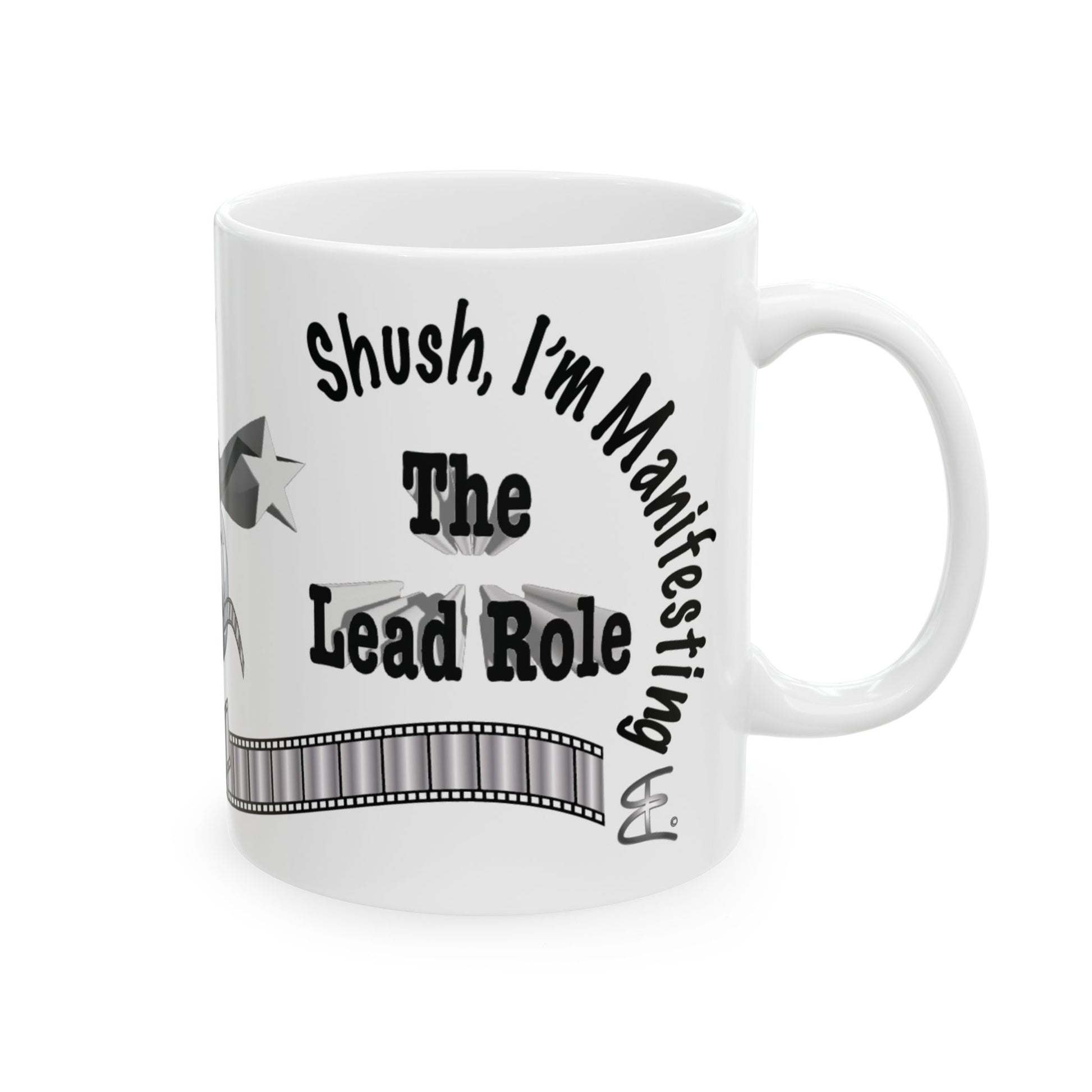 A white ceramic mug with a black printed graphic that reads 'Shush, I'm Manifesting The Lead Role' with a film strip design, shown on a plain white background.