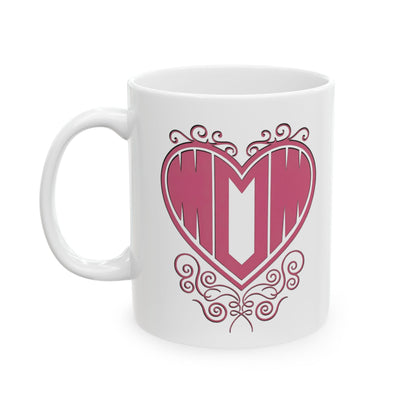 White ceramic mug with "Mom" printed in pink text inside a heart with decorative filigree, on a white background.