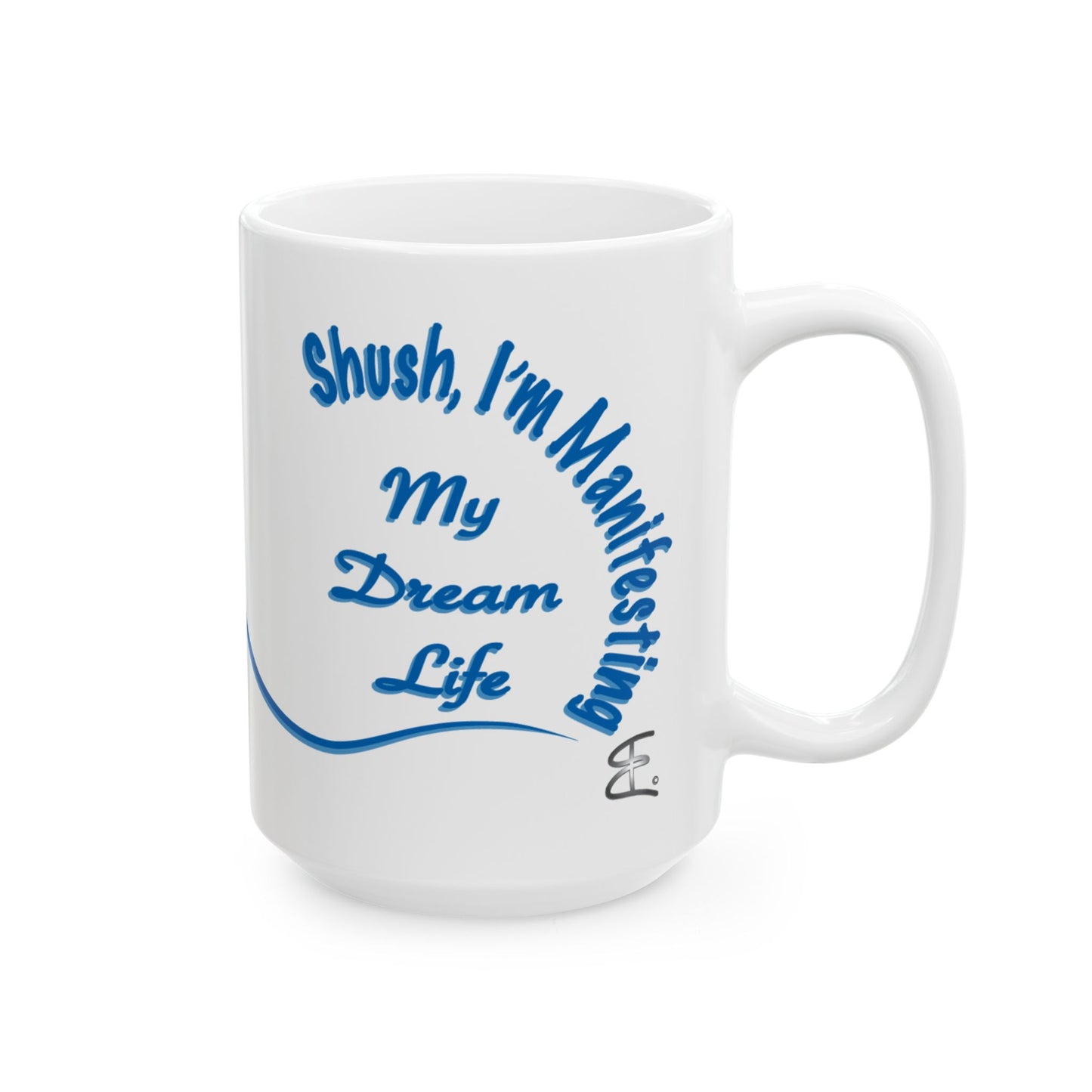 A white ceramic mug with blue text that reads 'Shush, I'm Manifesting My Dream Life' and a small signature-style mark near the bottom right of the design, shown on a plain white background.