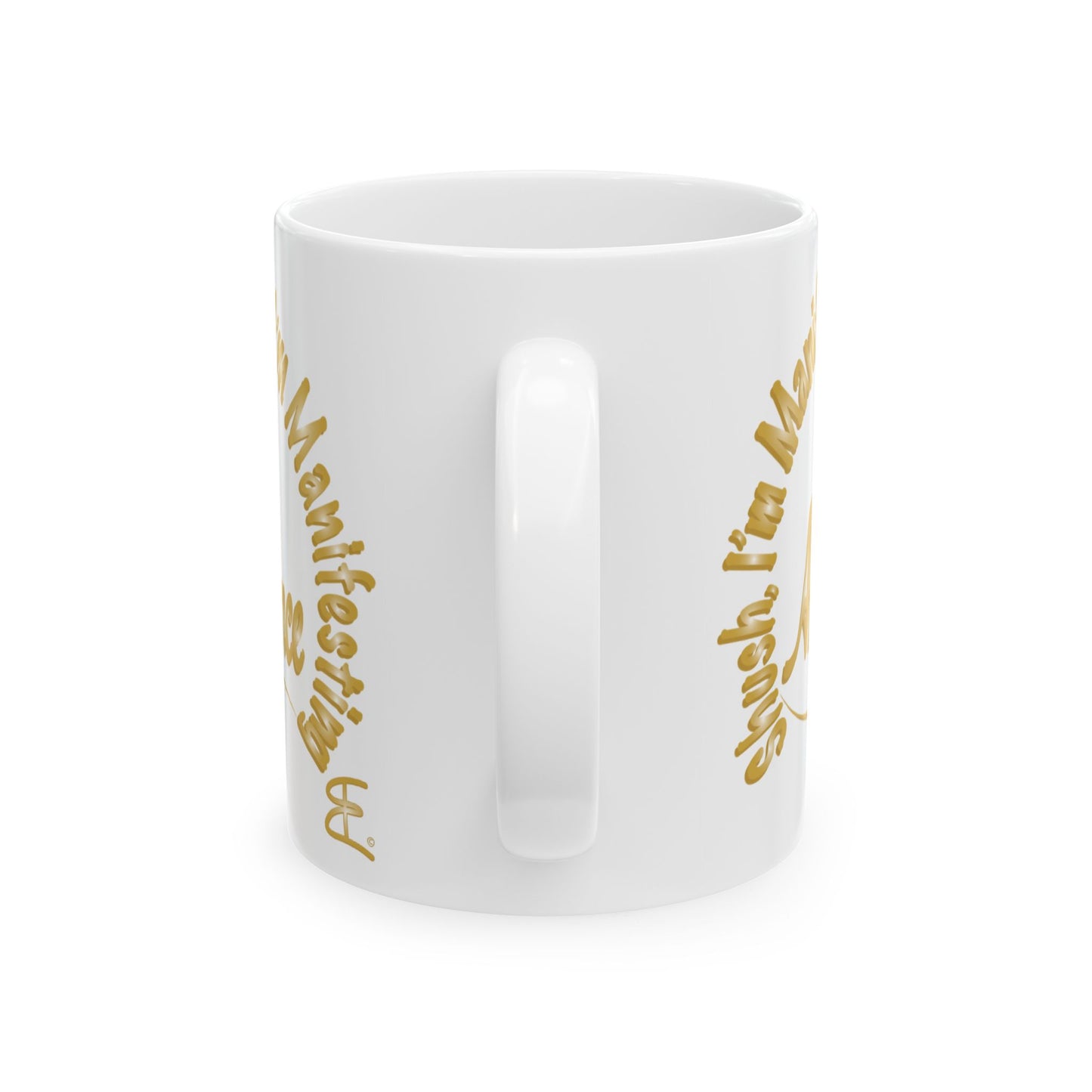 A white ceramic mug with a glossy finish, featuring gold text that reads 'Shush I'm Manifesting Abundance' on both sides, shown against a plain white background.