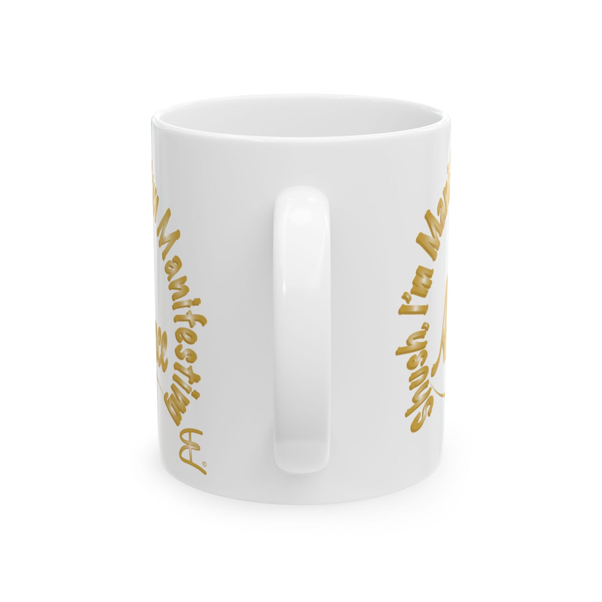 A white ceramic mug with a glossy finish, featuring gold text that reads 'Shush I'm Manifesting Abundance' on both sides, shown against a plain white background.