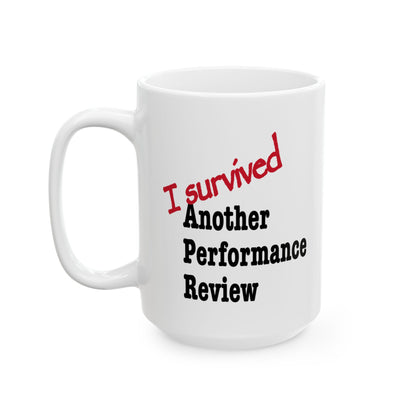 Detail shot of glossy "I Survived Another Performance Review" ceramic coffee cup with strong sarcastic workplace message

