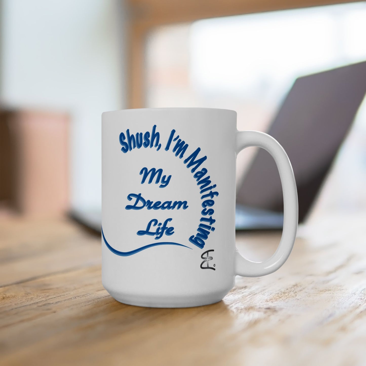 White mug with blue Shush, 'I'm Manifesting My Dream Life', text on a wooden surface