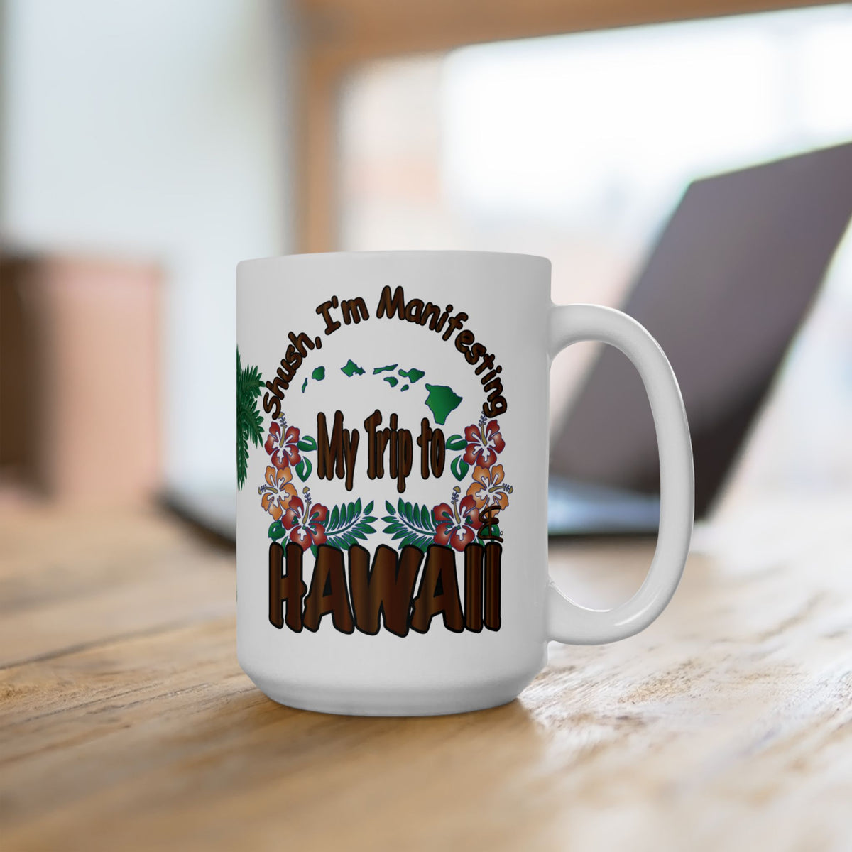 A white ceramic coffee mug with a colorful graphic design that reads 'Sush, I'm Manifesting My Trip to HAWAII' with tropical flowers and green islands, sitting on a wooden table with a blurred laptop in the background.