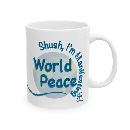 A white ceramic mug, right handle view with a blue and light blue graphic design that reads 'Shush, I'm Manifesting World Peace' over a globe illustration, shown on a plain white background.
