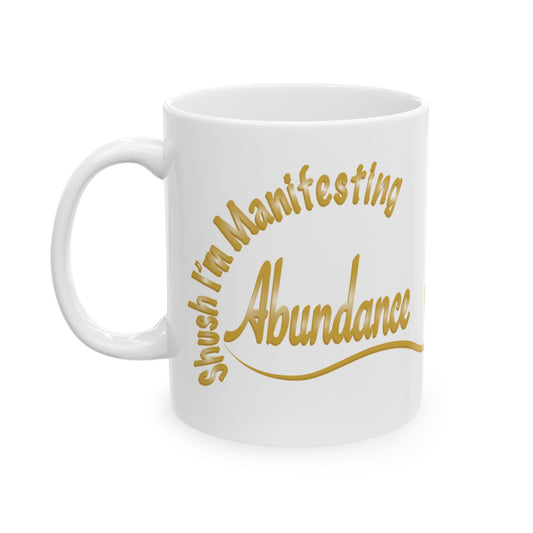 White ceramic mug with the text 'Shush, I'm Manifesting Abundance'

