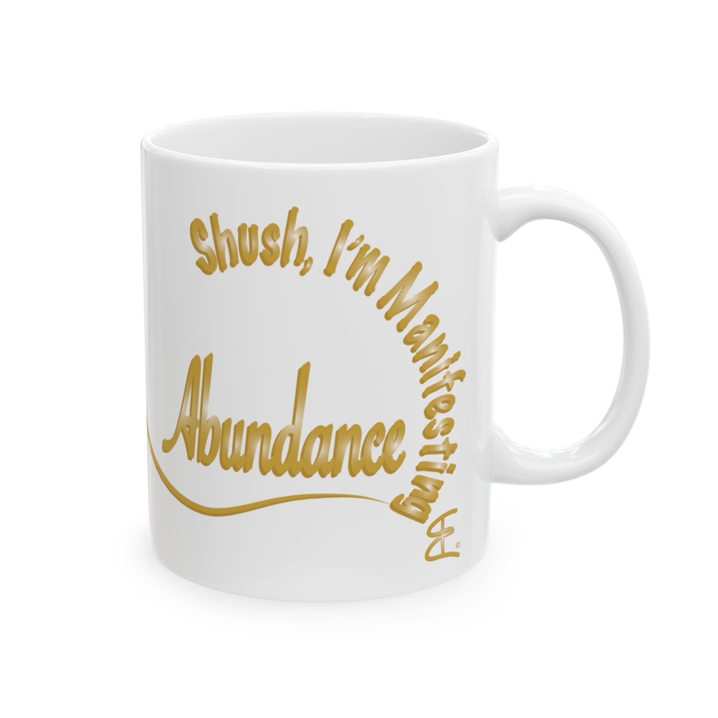 A white ceramic mug with a gold print that reads 'Shush, I'm Manifesting Abundance' on a clean white background.
