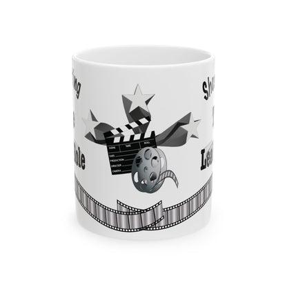 A white ceramic mug featuring a black and gray graphic design with a clapperboard, film reel, stars, and a film strip, with partial text showing.