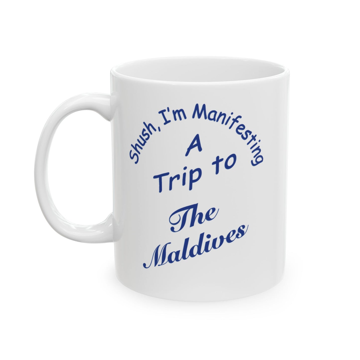 A white ceramic coffee mug with blue printed text that reads 'Shush, I'm Manifesting A Trip to The Maldives' on a clean white background.