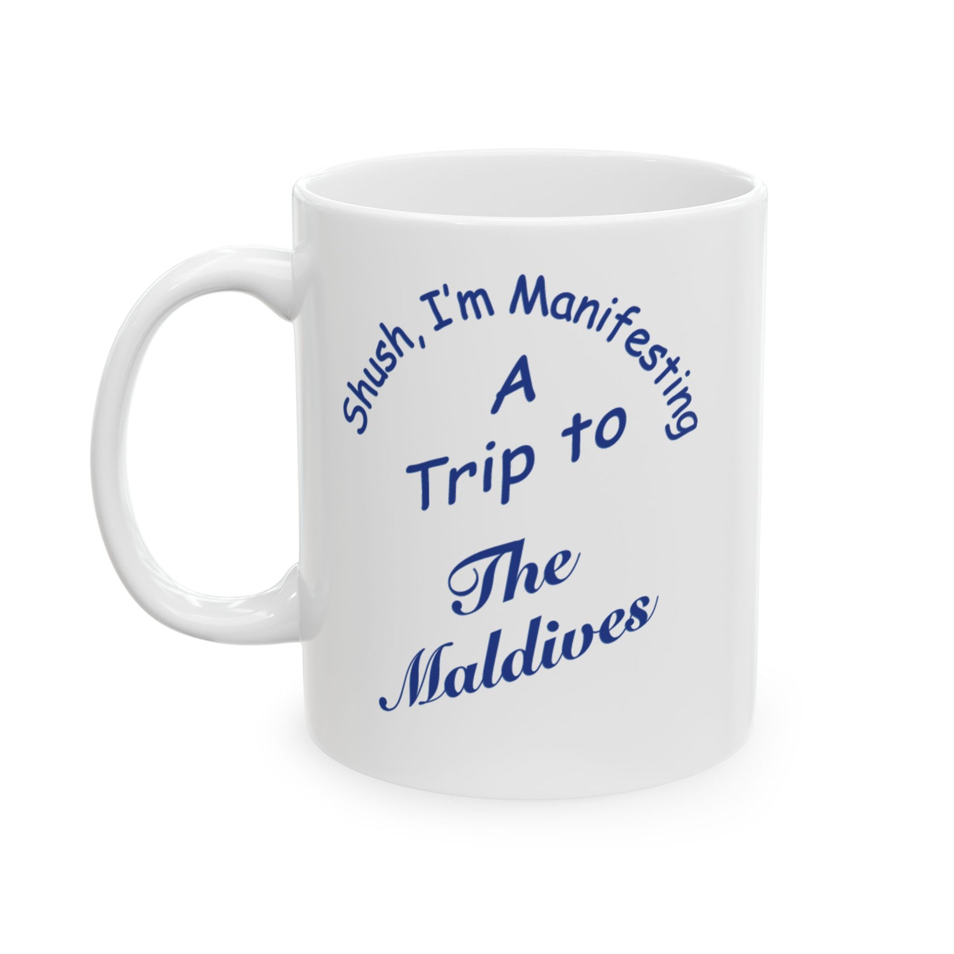 A white ceramic coffee mug with blue printed text that reads 'Shush, I'm Manifesting A Trip to The Maldives' on a clean white background.