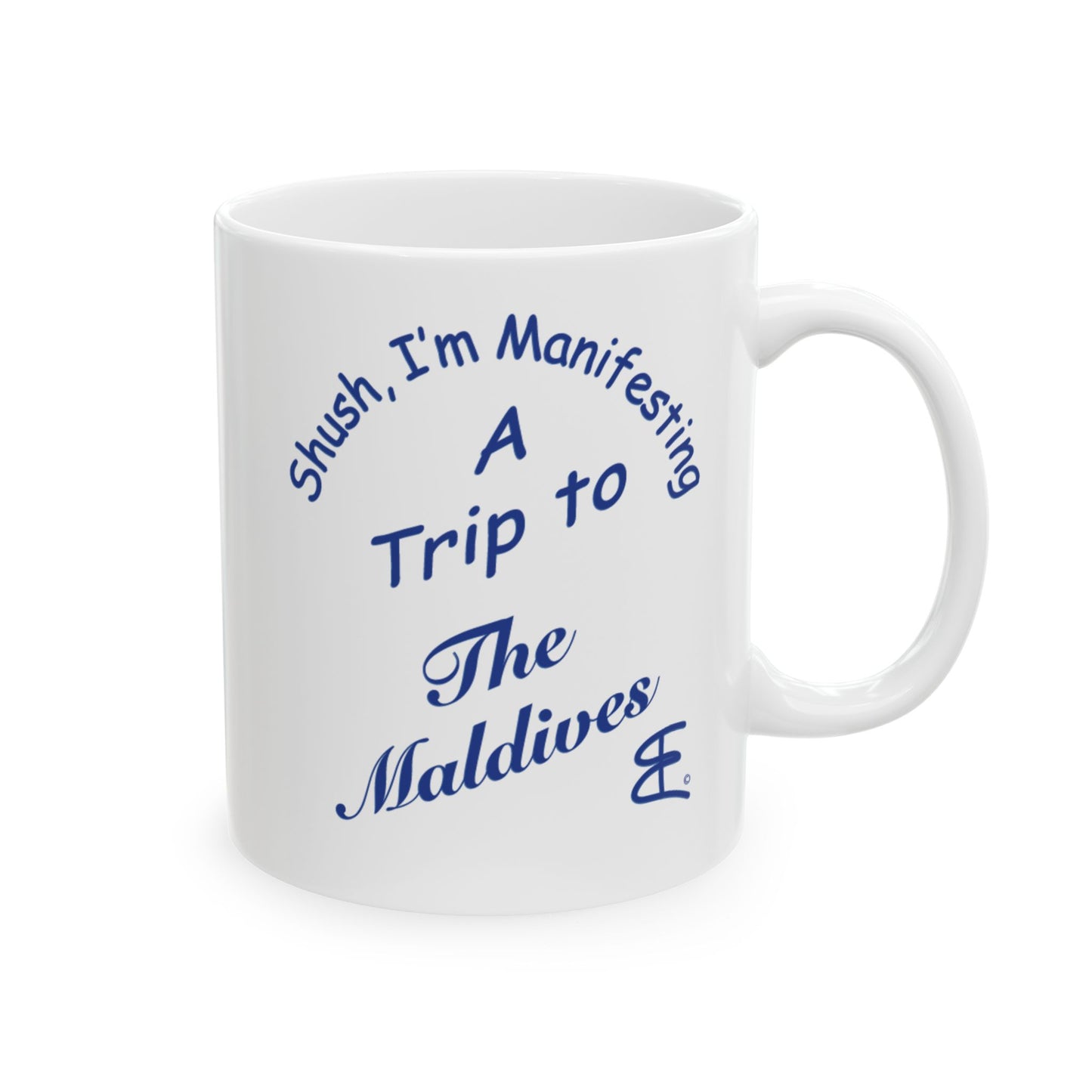A white ceramic mug with blue printed text that reads 'Shush, I'm Manifesting A Trip to The Maldives' on a clean white background.