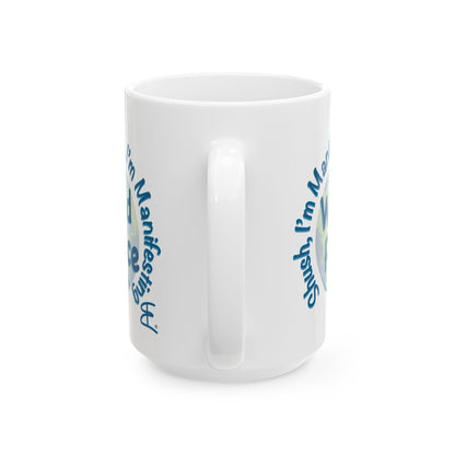 A white ceramic mug with a blue, light blue and green graphic design that reads 'Shush I'm Manifesting World Peace' on a clean white background.