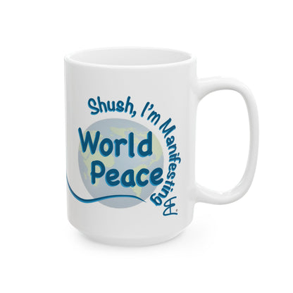 A white ceramic coffee mug with a blue and light blue graphic design on the front. The design features the text 'Shush, I'm Manifesting World Peace' in blue lettering over a circular globe graphic.