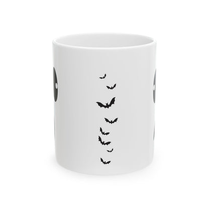 A white ceramic mug featuring a black graphic print of flying bats and partial circular eye designs on the sides, shown against a plain white background.