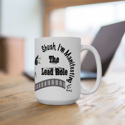 White mug with text 'Shush, I'm Manifesting The Lead Role' on a wooden surface.