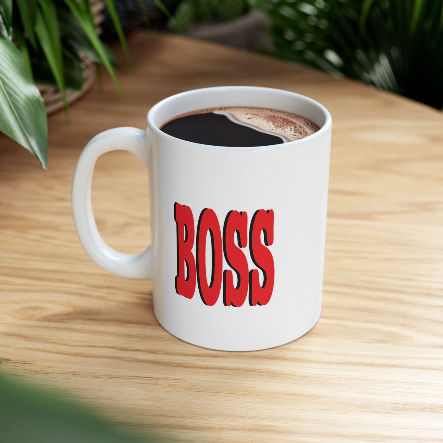 A white ceramic mug sits on a light wood tabletop. The mug features the word 'BOSS' printed in large red letters.