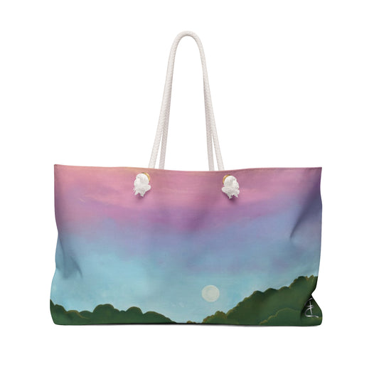 A tote bag featuring a pastel landscape print with a pink and purple sky, blue gradient, green trees, and a white moon, complete with white rope handles.