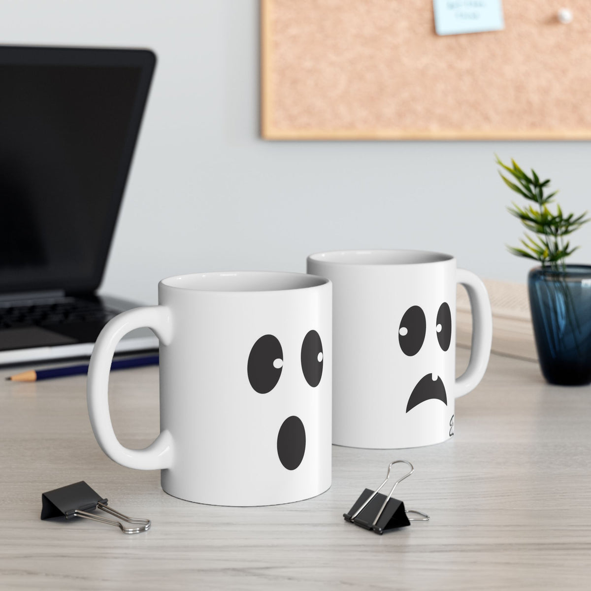Two mugs with ghost face designs on a desk with office supplies and a plant.