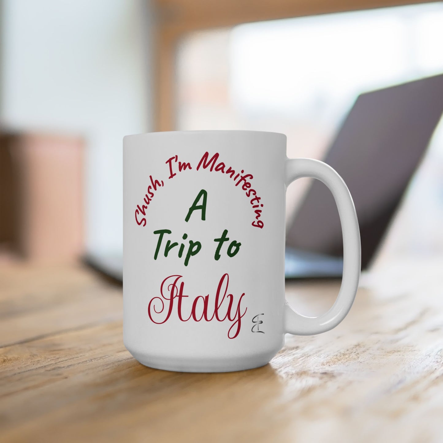 White mug with text 'Shush, I'm Manifesting A Trip to Italy' on a wooden surface.
