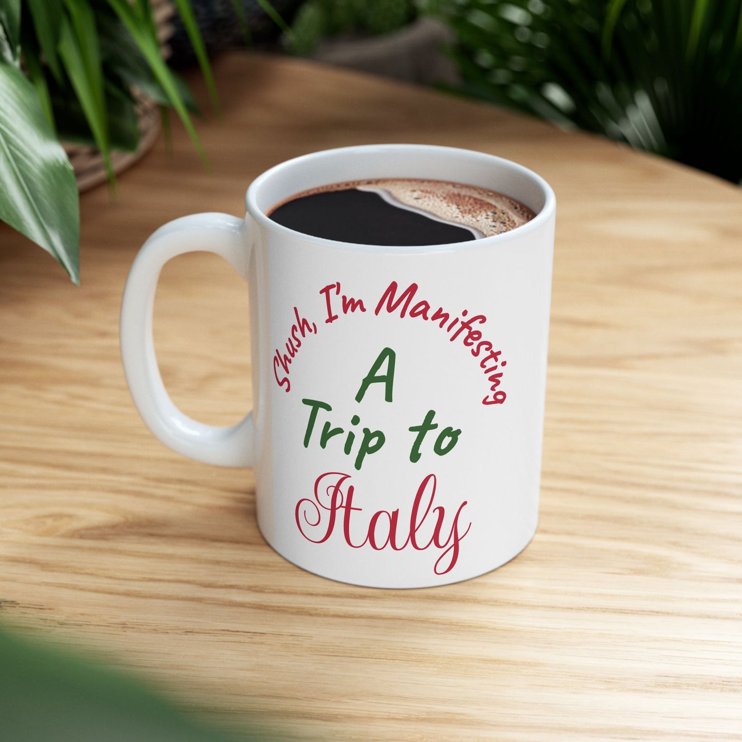 White mug with text 'Such, I'm Manifesting A Trip to Italy' on a wooden table.