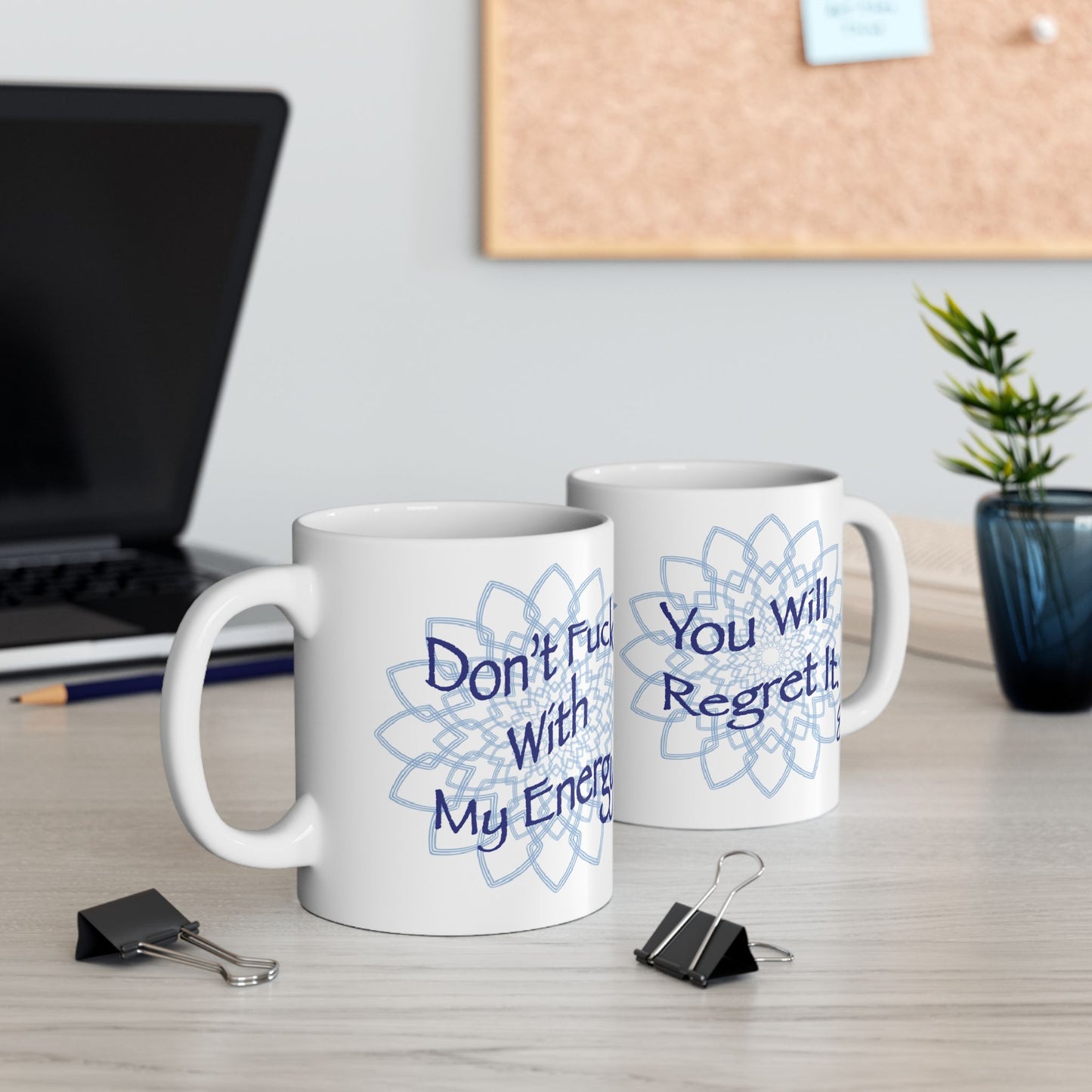 Two white mugs showing what this mug looks like on both sides, one says Don't Fuck With My Energy and the other says, You Will Regret it, on a desk with office supplies.
