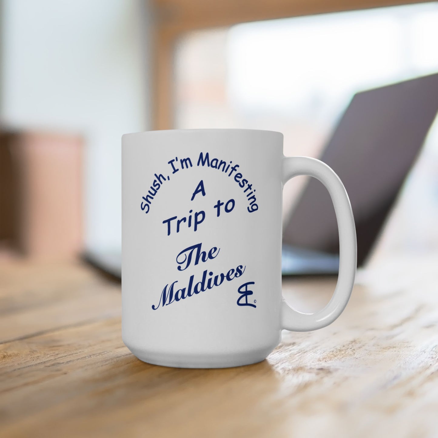 White mug with 'Shush I'm Manifesting A Trip to The Maldives' text on a wooden surface.