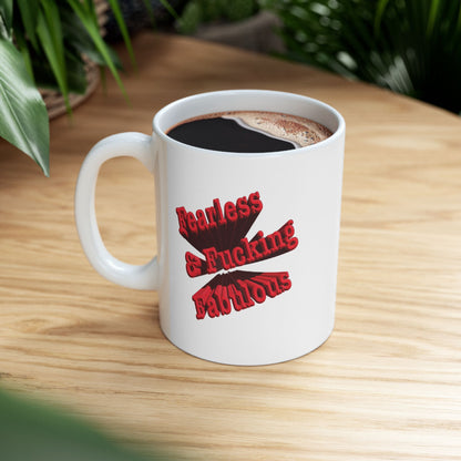 A white ceramic mug with a red graphic text design that reads 'Fearless & Fucking Fabulous' sitting on light wooden desk.
